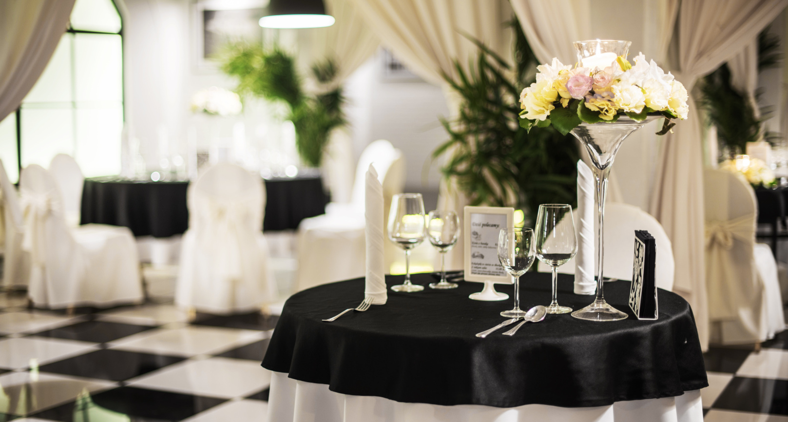 Elegant hotel restaurant table with black tablecloth, white chairs, floral centerpiece, and polished glassware in a bright dining room.