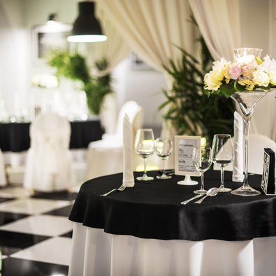 Eleganter Hotel-Restauranttisch mit schwarzem Tischtuch, weißen Stühlen, Blumenarrangement und poliertem Glasgeschirr in hellem Speisesaal.
