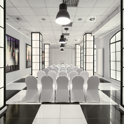 Elegancka sala konferencyjna z białymi krzesłami w rzędach, czarno-białą podłogą i nowoczesnym oświetleniem