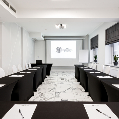 Moderner Konferenzraum mit schwarzen Tischdecken, weißen Stühlen, Marmorboden, Beamer und Leinwand für Präsentationen.