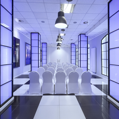 Conference room with rows of white chairs, blue-lit pillars, and modern ceiling lights creating a sleek ambiance.