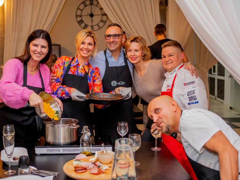 Group of smiling people cooking in a hotel kitchen, with cheese board and wine glasses on the table