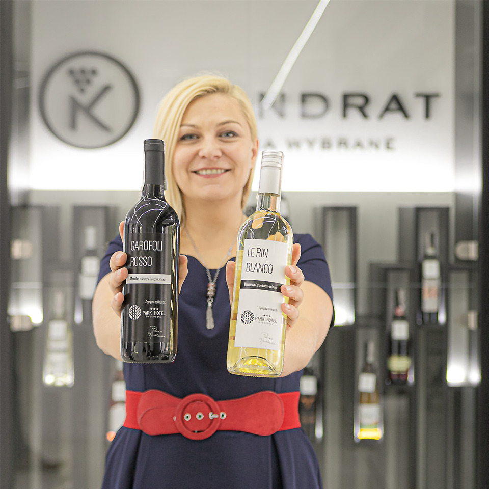 Smiling woman holding red and white wine bottles in a stylish hotel wine shop