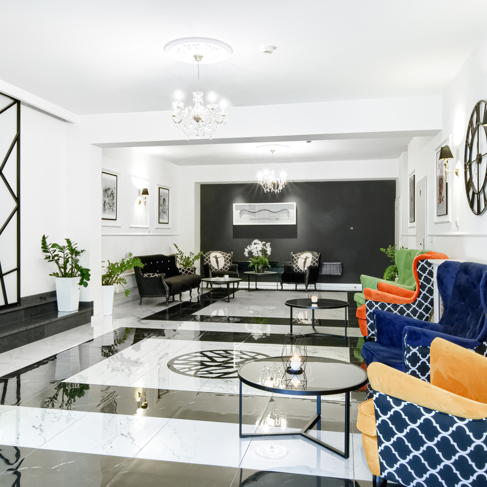 Modern hotel lounge with glossy black and white marble floor, designer armchairs in bold colors, and crystal chandeliers