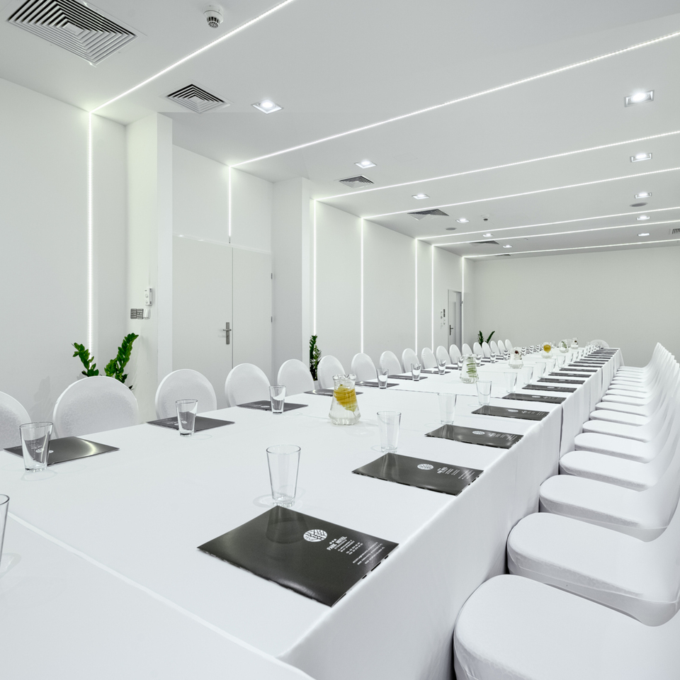 Elegantní konferenční místnost s bílými ubrusy, židlemi a dokumenty připravenými na pracovní schůzku.