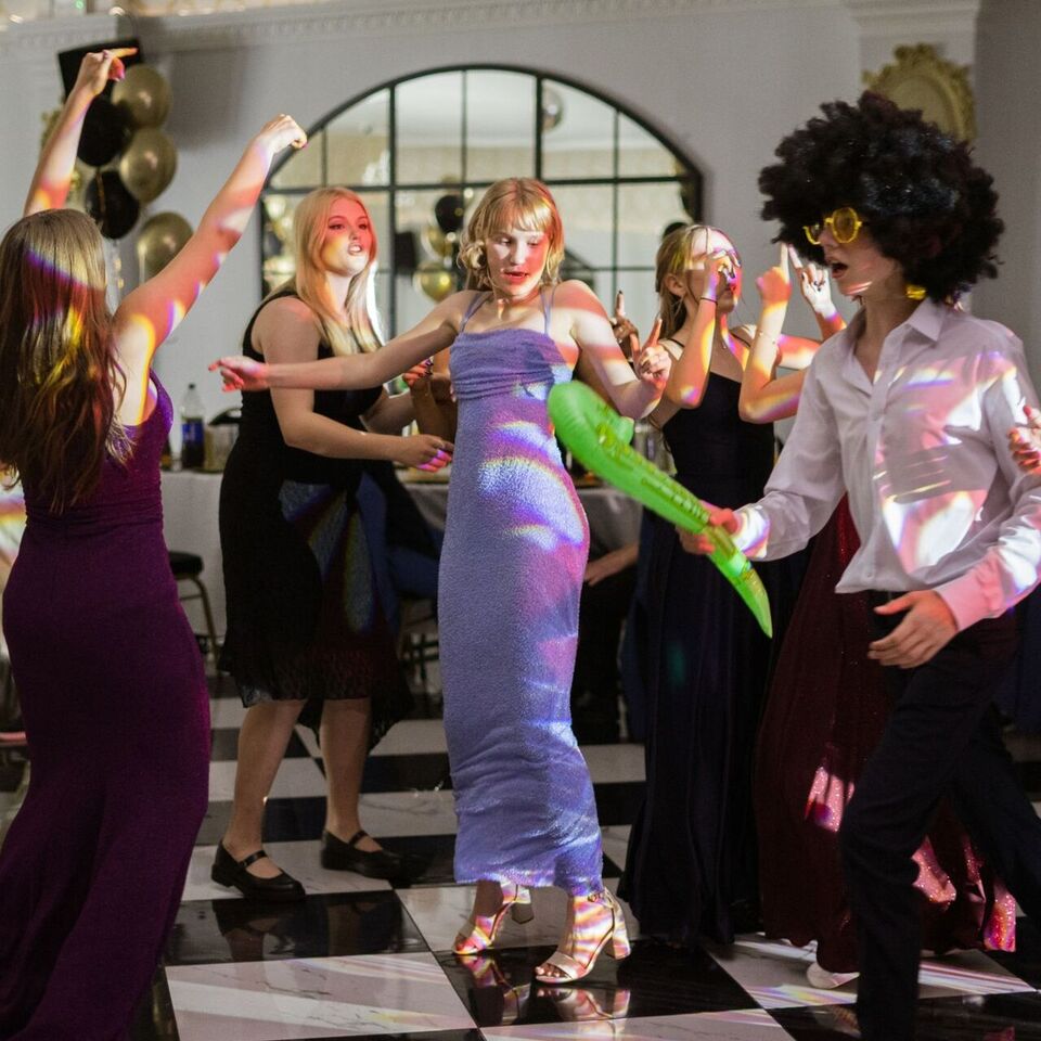 Guests dancing at a lively party in an elegant hall with mirrored walls and festive balloon decorations.