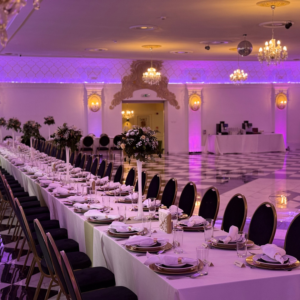 Eleganter Hotelfestsaal für Bankett – lange Tafeln mit Blumenarrangements, Kronleuchtern, violetter Beleuchtung und Marmorboden.