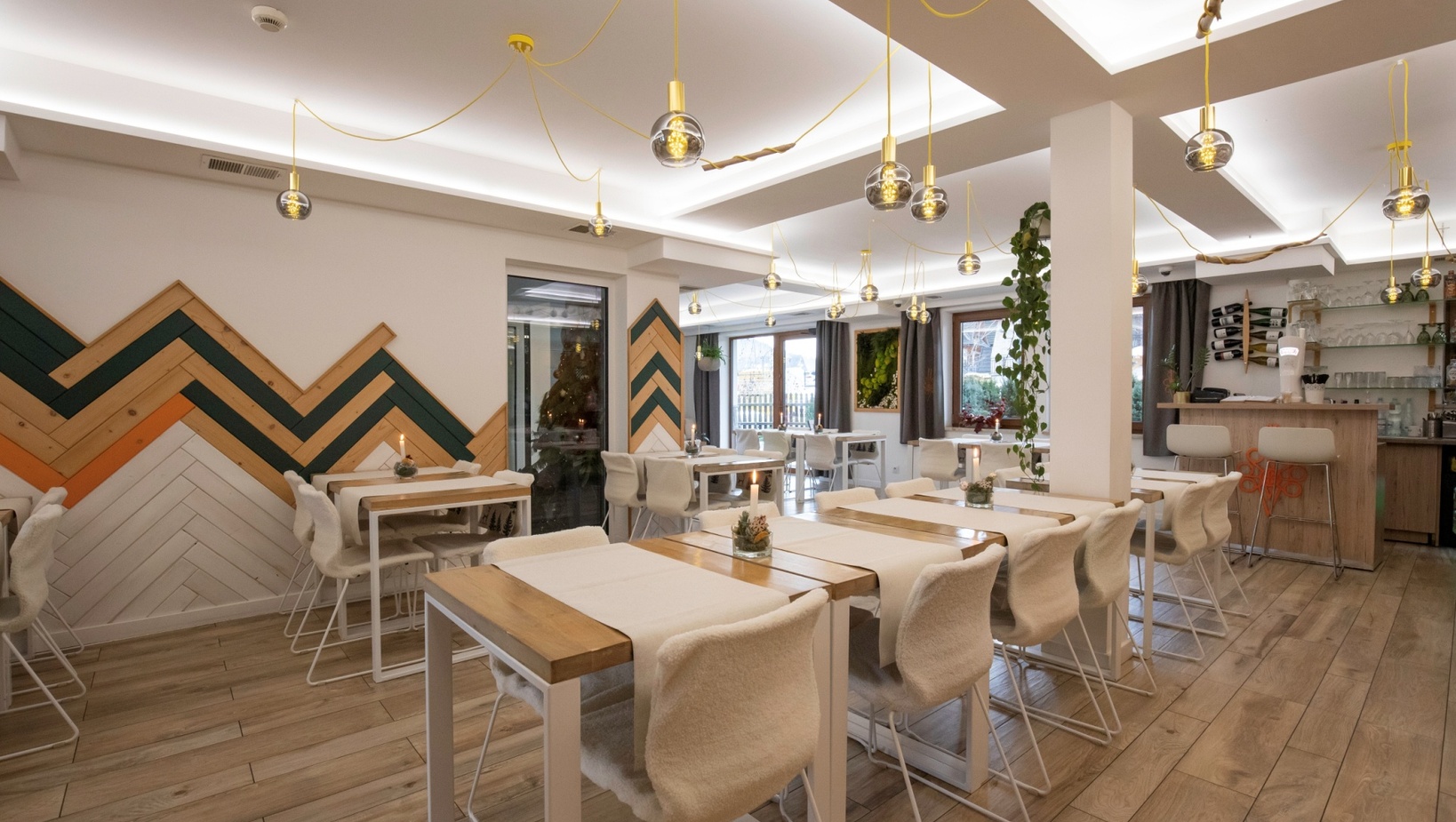 Przytulna restauracja z drewnianymi stołami, futrzanymi krzesłami, szklanymi lampami na żółtych przewodach, barem, oknami i dekoracyjną ścianą