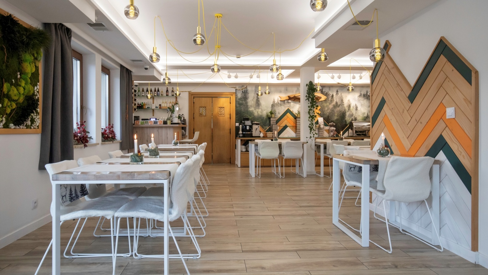 Przytulna restauracja hotelowa z jasnymi drewnianymi stołami, miękkimi narzutami na krzesłach, szklanymi lampami, muralem lasu i barem.