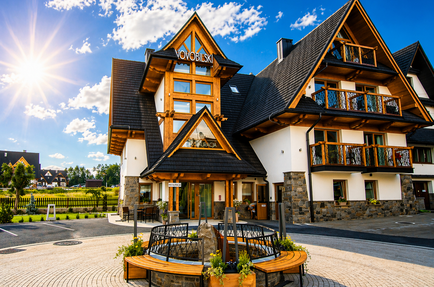Hotel w stylu alpejskim z drewnianymi belkami i balkonami, słoneczny dziedziniec z ławkami, fontanną i restauracją