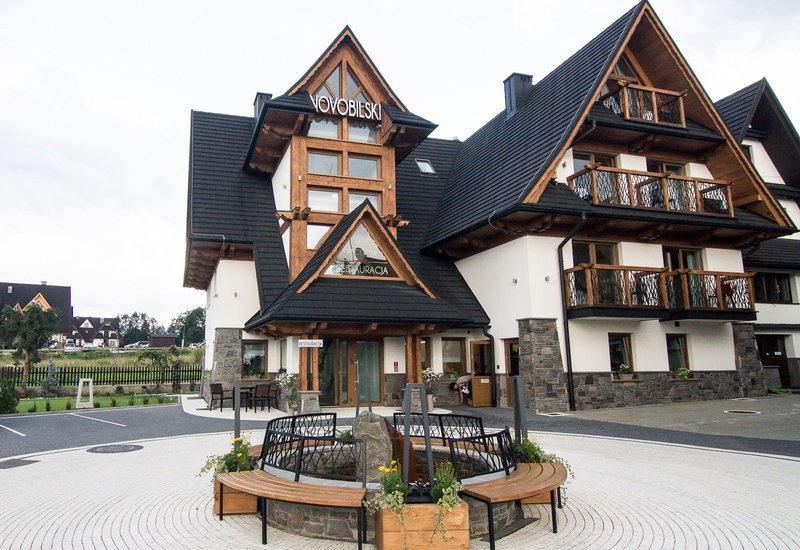 Górski pensjonat w stylu zakopiańskim z drewnianymi balkonami, kamienną podstawą, restauracją i fontanną na dziedzińcu.