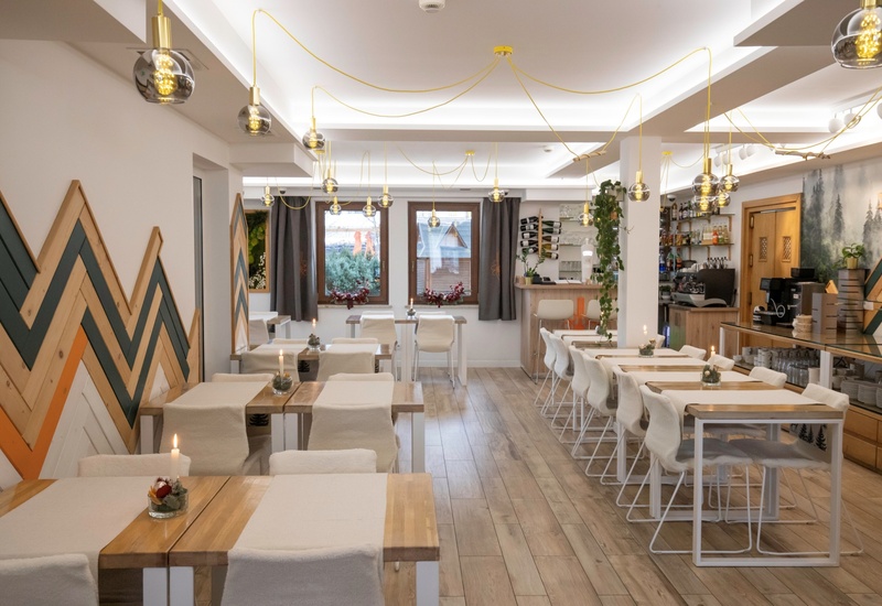 Kameralna restauracja hotelowa z drewnianymi stołami, miękkimi krzesłami, wiszącymi lampami i przytulnymi świecami przy barze.