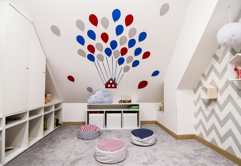Przytulny pokój zabaw na poddaszu z naklejkami balonów na suficie, pufami do siedzenia, półkami i zabawkami.