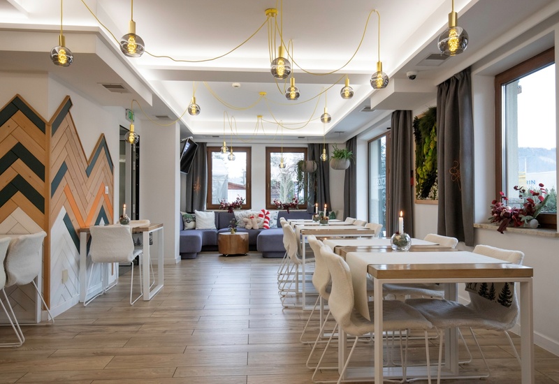 Przytulna jadalnia i salon z podświetlanymi kulistymi lampami, drewnianymi stolikami, futrzanymi krzesłami i dużymi oknami.
