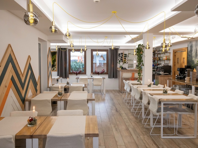 Kameralna restauracja hotelowa z drewnianymi stołami, miękkimi krzesłami, wiszącymi lampami i przytulnymi świecami przy barze.