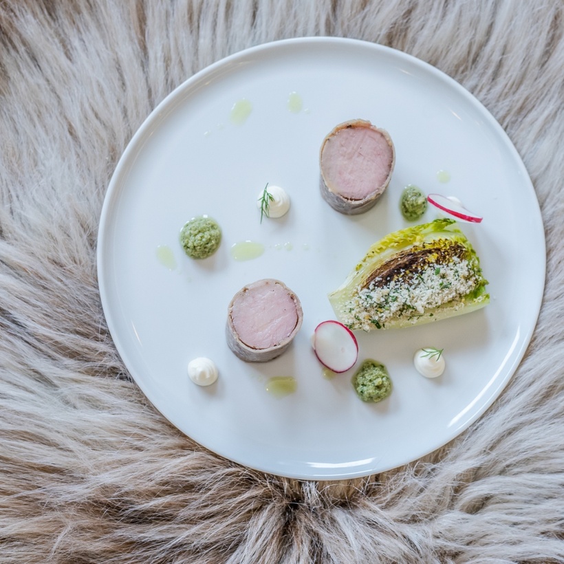 Wykwintne danie: plastry polędwicy owiniętej, grillowana sałata rzymska z kruszonką, plasterki rzodkiewki i kleksy pesto na białym talerzu