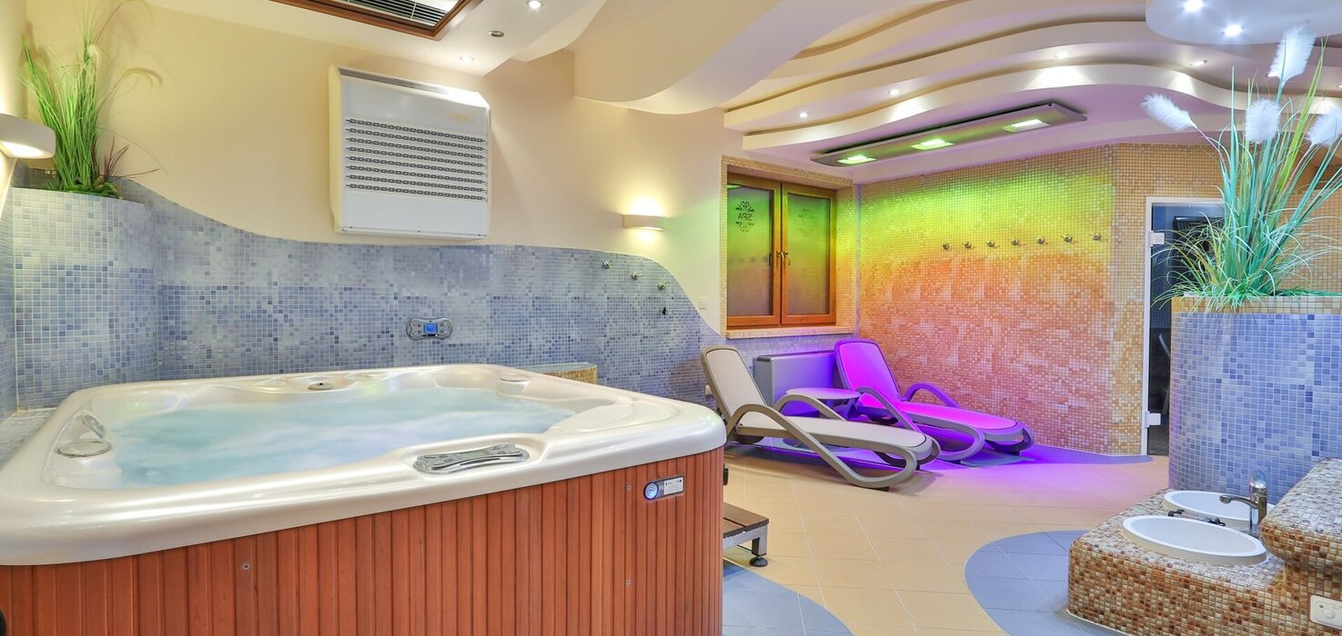 Wnętrze spa z jacuzzi, mozaikowymi ścianami, falistym sufitem, kolorowym oświetleniem i leżakami do relaksu