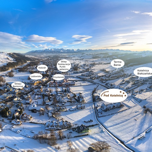 Panoramablick auf verschneites Dorf mit Chalets, sonnigen Skipisten, Bergkette und markierten Freizeitangeboten.