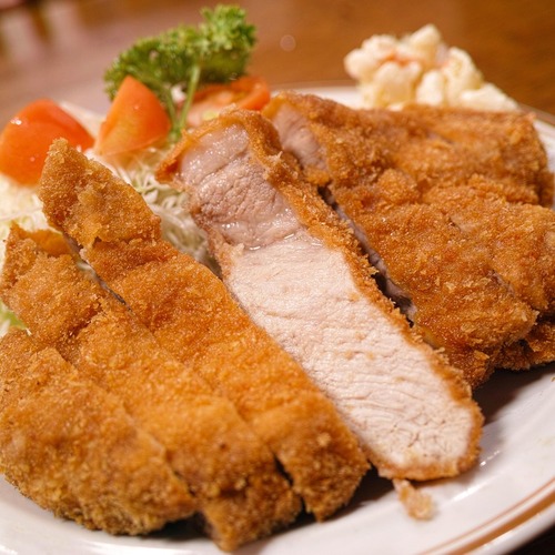 Knusprig paniertes, aufgeschnittenes Schnitzel mit fein gehobeltem Kohl, Tomate, Kartoffelsalat und Senf