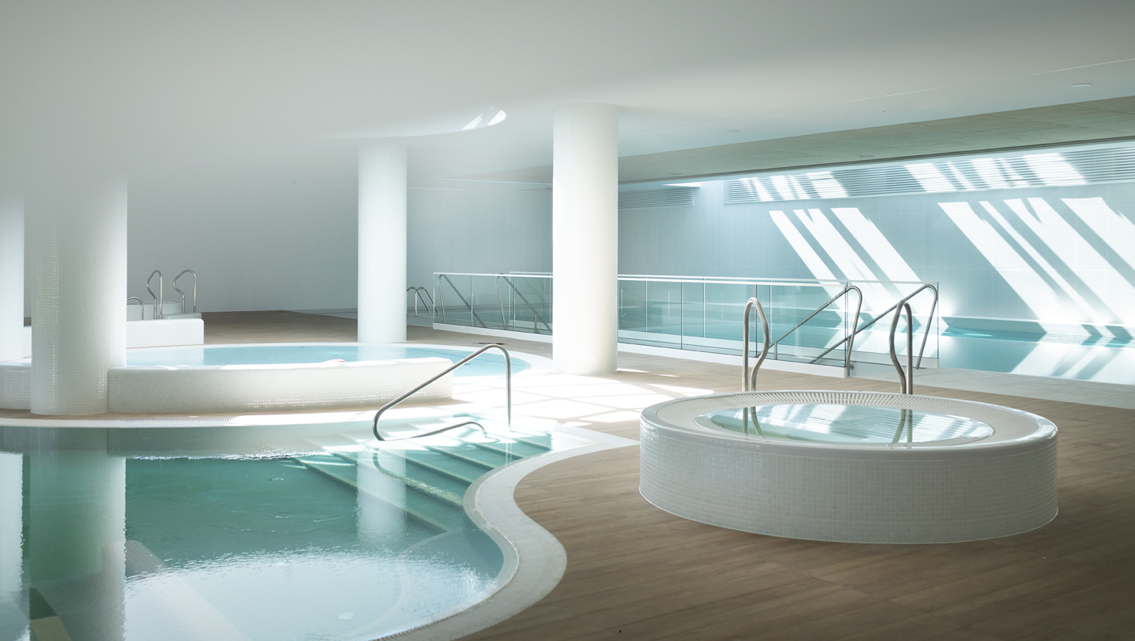 Przestronny, nowoczesny basen i jacuzzi w jasnym przestronnym wnętrzu hotelowego spa z białymi kolumnami i dużym światłem naturalnym