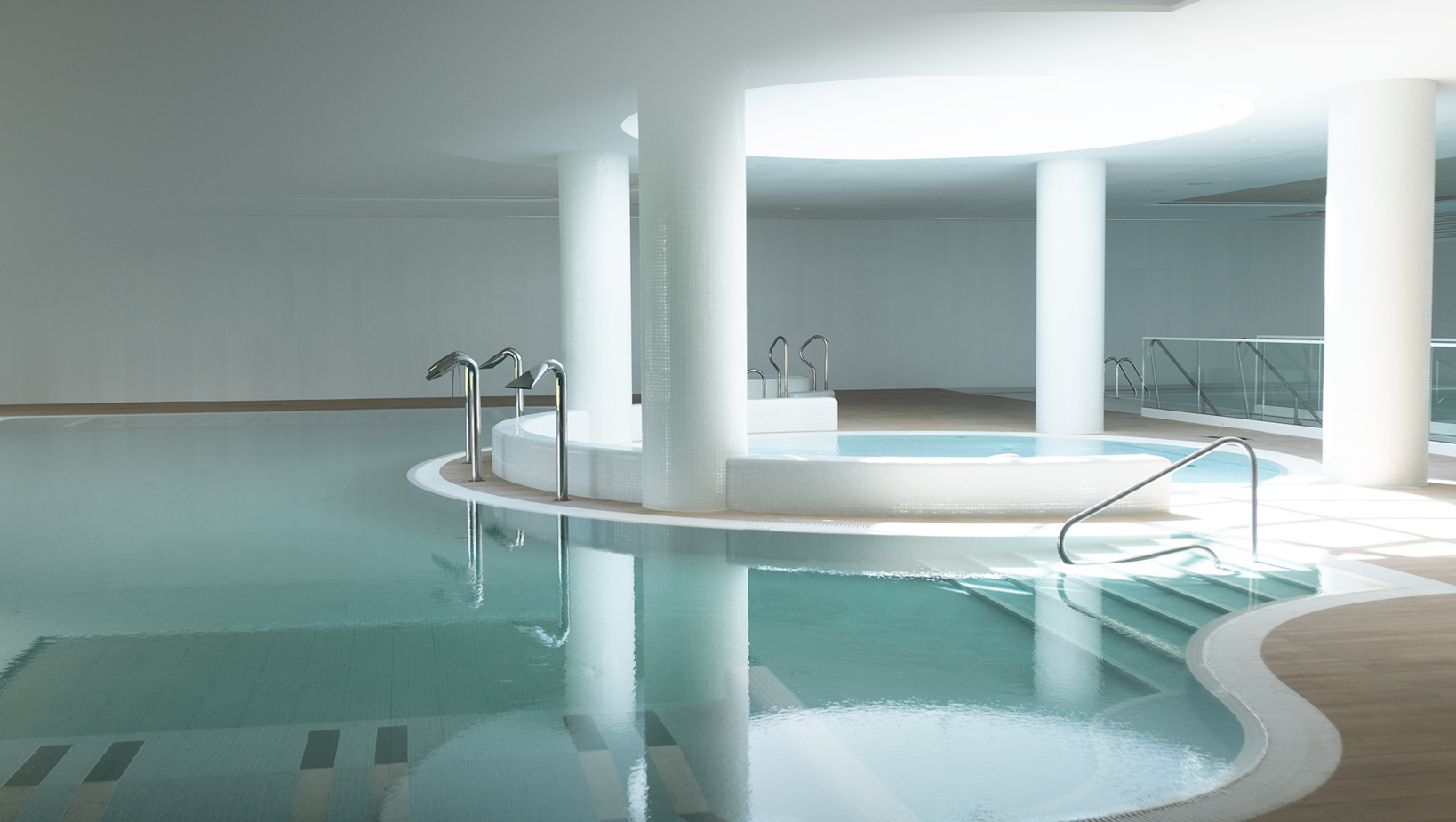 Nowoczesny, jasny basen wewnętrzny z jacuzzi i stylowymi poręczami, idealny na relaks i regenerację w spa hotelowym.