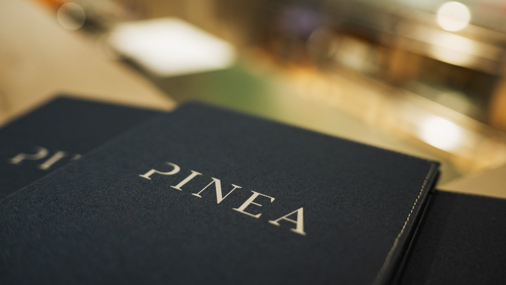 Eleganckie menu restauracji Pinea z granatową okładką na blacie baru.