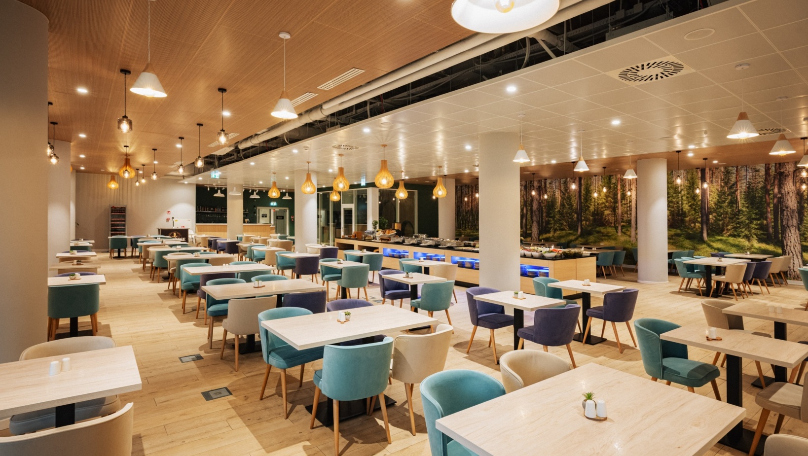 Elegancka restauracja hotelowa z jasnym drewnianym wnętrzem, miękkimi fotelami i bufetem z dekoracjami roślinnymi.