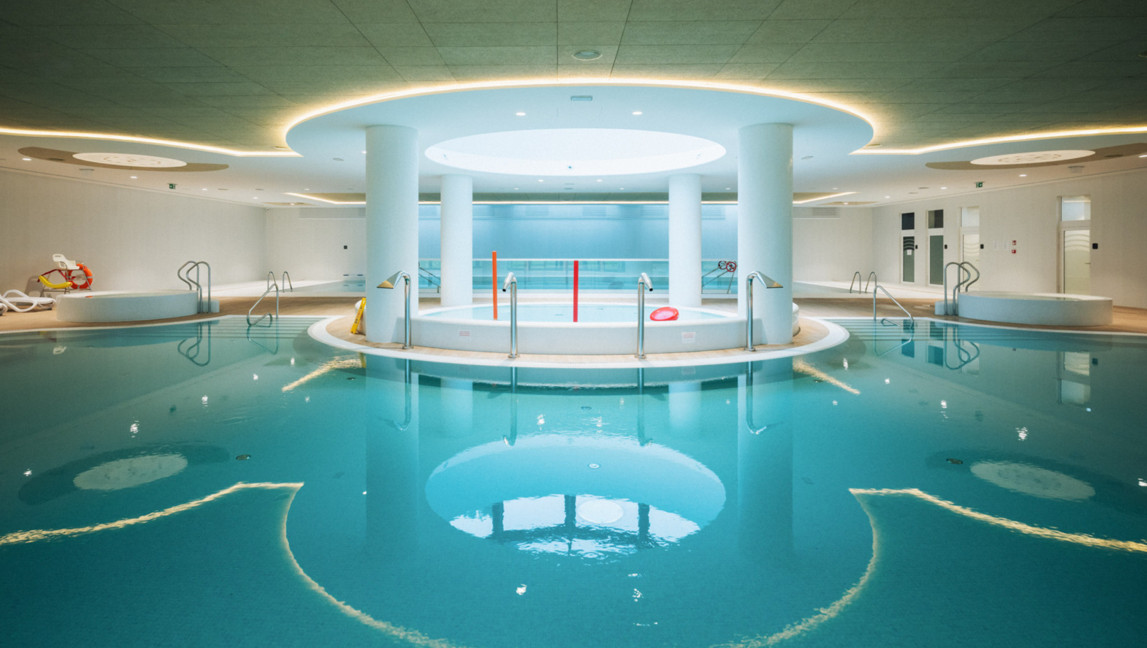 Nowoczesny hotelowy basen wewnętrzny z centralnym jacuzzi, jasnym oświetleniem i minimalistycznym designem