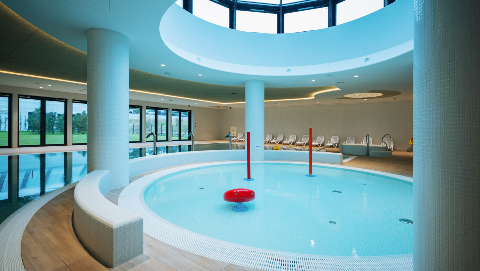 Nowoczesny hotelowy basen kryty z okrągłą niecką dla dzieci i panoramicznym oknem w suficie, leżaki w tle