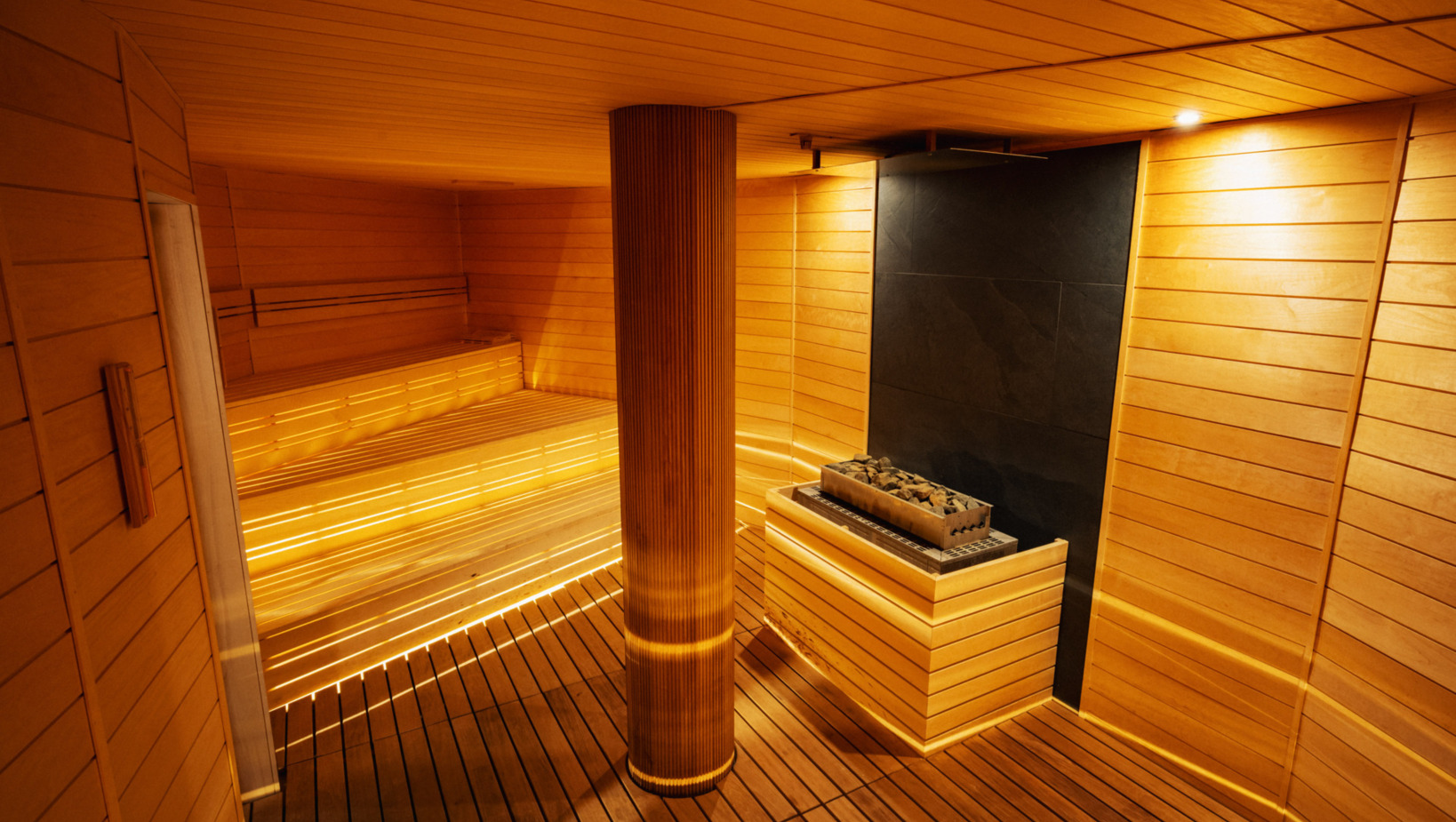 Nowoczesna sauna hotelowa z drewnianymi ławkami, nastrojowym oświetleniem i piecem z kamieniami do sauny.