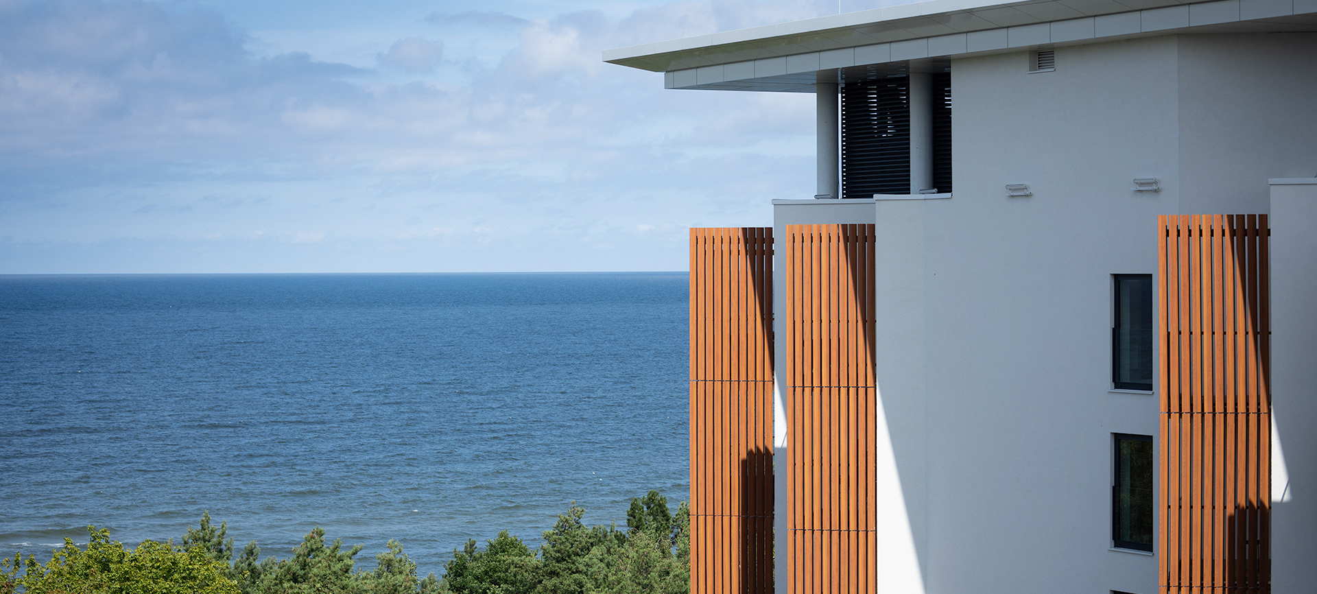 Modernes Hotel mit Holzverkleidung und Blick auf das Meer sowie grüne Kiefern