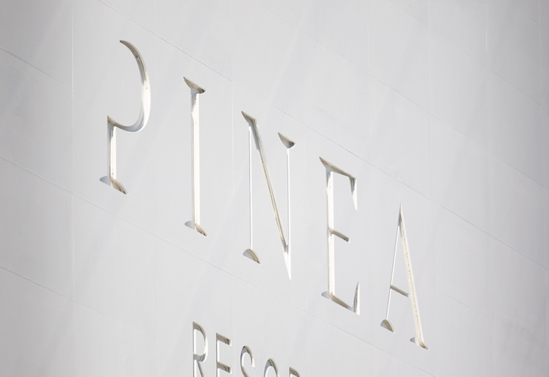 Biała ściana z nazwą hotelu Pinea Resort w nowoczesnym, minimalistycznym stylu