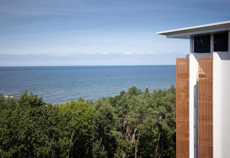 Widok na morze i las sosnowy z nowoczesnego hotelu z białą fasadą i drewnianymi panelami