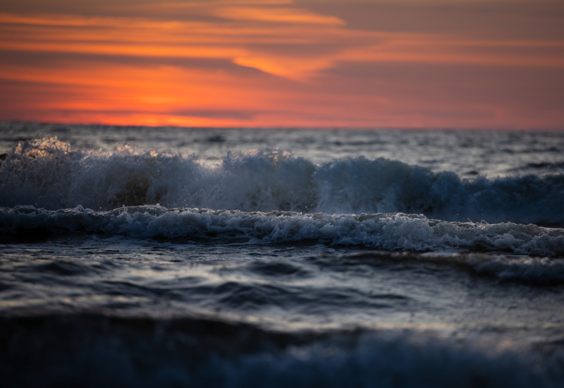 Fale morskie rozbijające się o brzeg podczas pomarańczowego zachodu słońca nad horyzontem