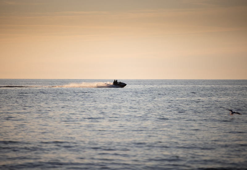 Dwie osoby na skutere wodnym pływają w słoneczny wieczór po spokojnym morzu przy zachodzie słońca.