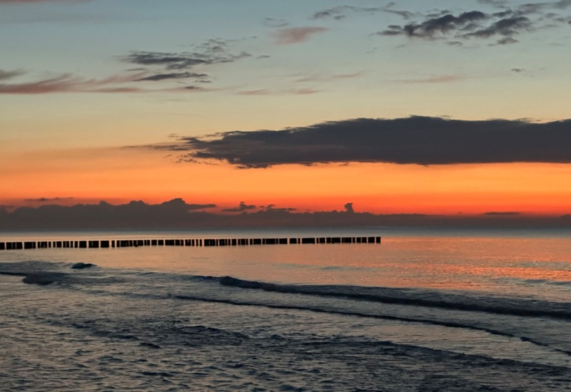 Spokojny zachód słońca nad morzem z faleami i drewnianymi groblami na horyzoncie