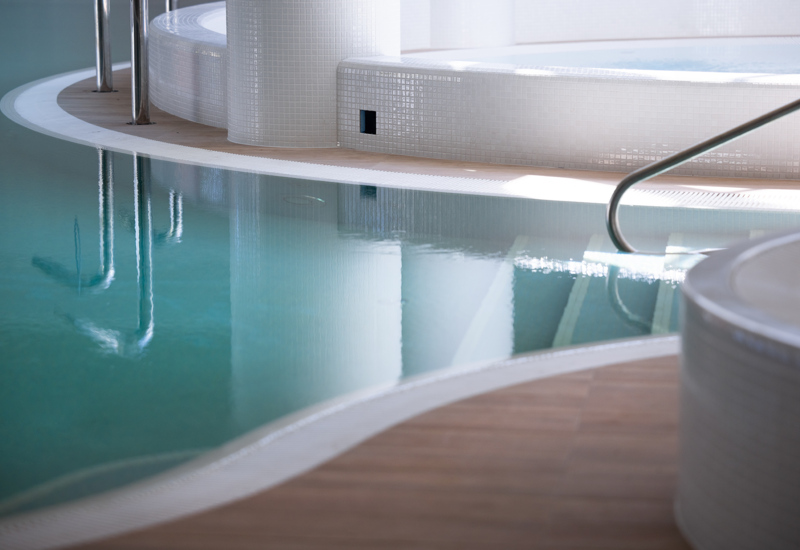 Wewnętrzny basen hotelowy z łagodnie zakrzywionymi białymi kafelkami i drewnianą podłogą dla relaksu gości.