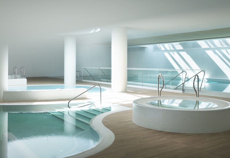 Przestronny, nowoczesny basen i jacuzzi w jasnym przestronnym wnętrzu hotelowego spa z białymi kolumnami i dużym światłem naturalnym