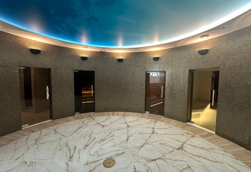 Luksusowa strefa spa z marmurową podłogą, mozaikowymi ścianami i drzwiami do saun oraz gabinetów zabiegowych