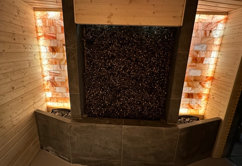 Sauna z drewnianymi panelami i ścianą z podświetlonych płyt soli himalajskiej tworząca relaksującą atmosferę.