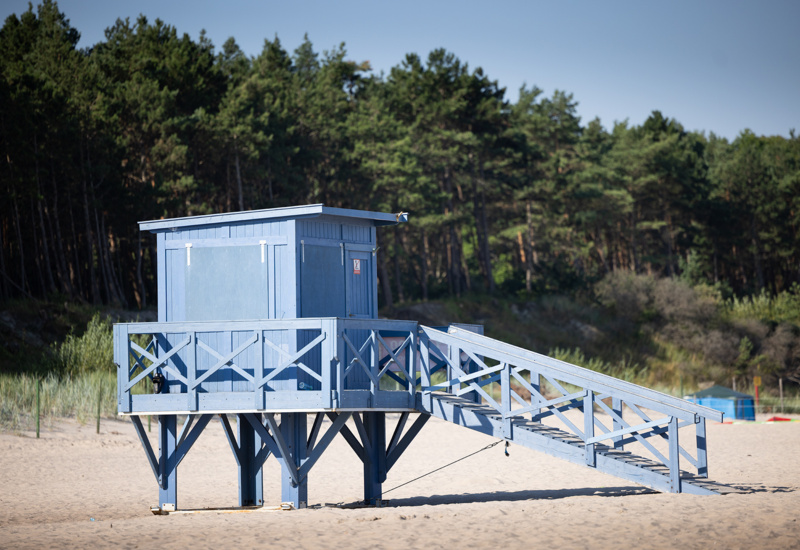 Niebieska drewniana stacja ratownika na piaszczystej plaży z widokiem na zielony las sosnowy