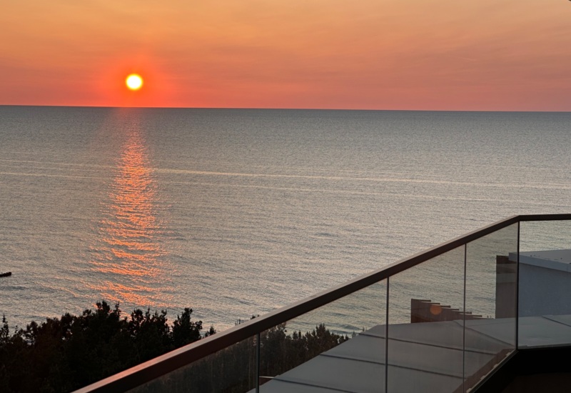 Widok na zachód słońca nad spokojnym morzem z tarasu hotelowego z przezroczystą barierką