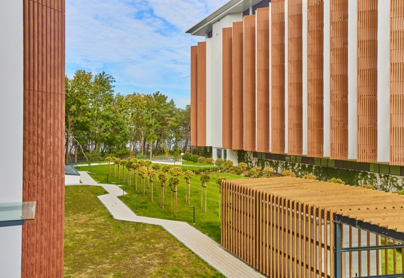 Nowoczesny hotel z fasadą z drewnianych paneli i zadbanym ogrodem z alejkami oraz młodymi drzewami