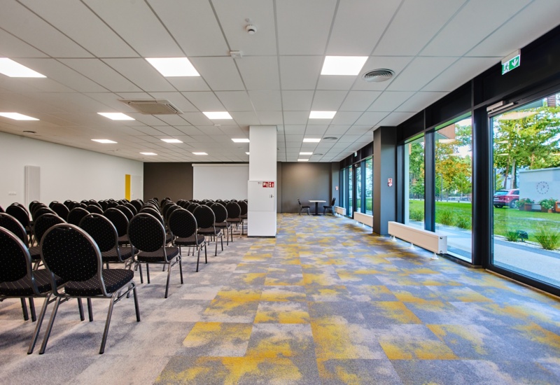 Nowoczesna sala konferencyjna z rzędem krzeseł i dużymi oknami z widokiem na zieleń na zewnątrz