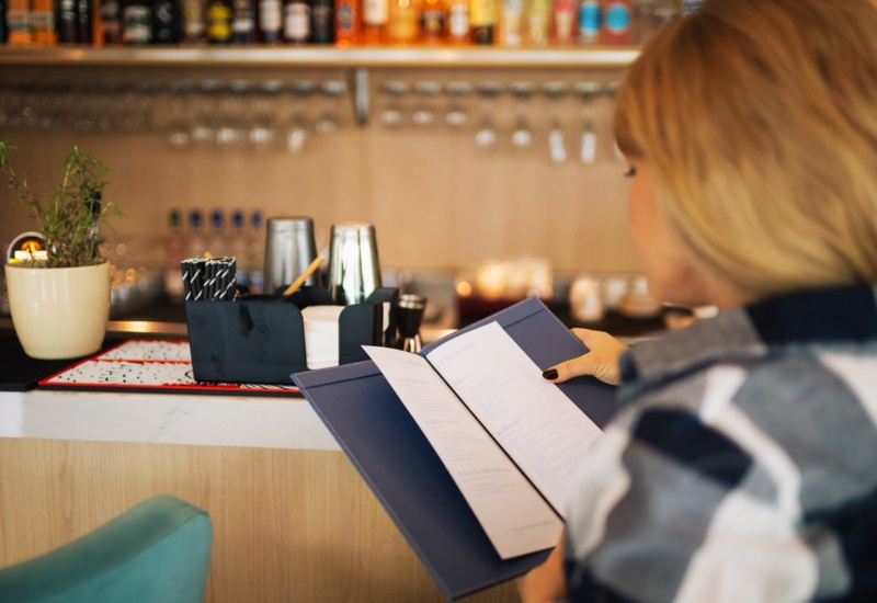 Gośćka przegląda menu w hotelowym barze z nowoczesnym wystrojem i roślinną dekoracją przy ladzie