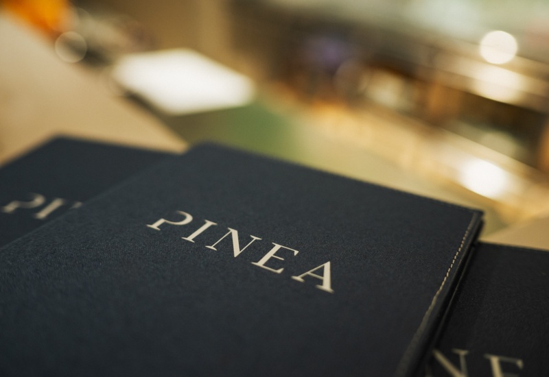 Eleganckie menu restauracji Pinea z granatową okładką na blacie baru.