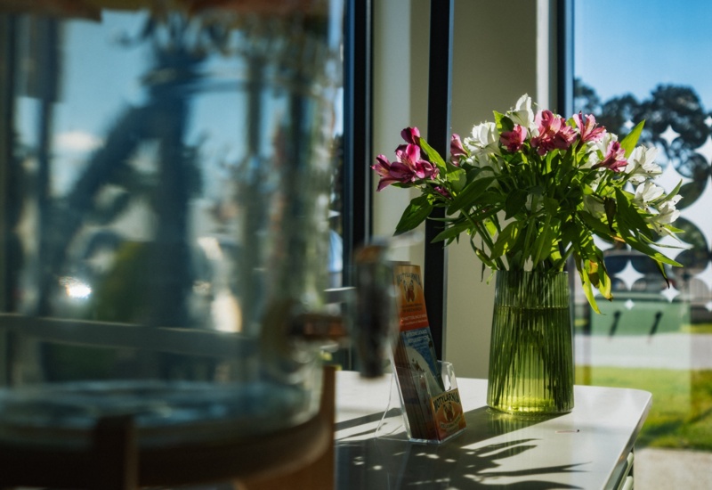 Wazon z różowymi i białymi kwiatami ustawiony na białym blacie przy oknie hotelowym z widokiem na zielony ogród