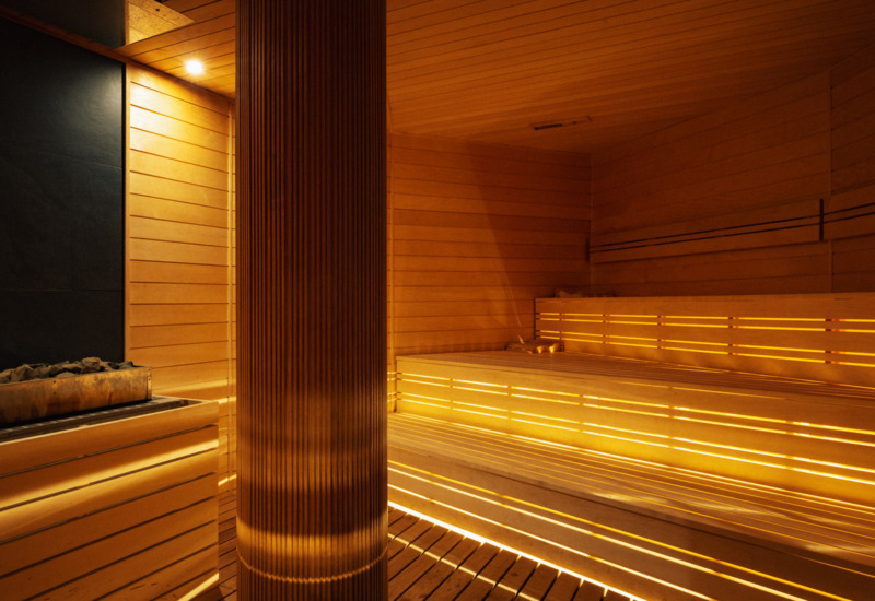 Nowoczesna sauna hotelowa z podświetlanymi drewnianymi ławami i stonowanym, ciepłym oświetleniem relaksacyjnym