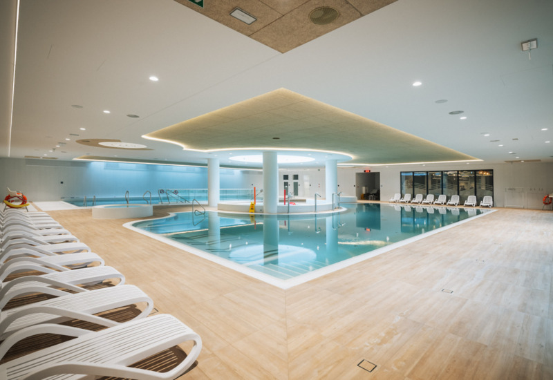 Przestronny, nowoczesny kryty basen hotelowy z leżakami i nastrojowym oświetleniem sufitowym
