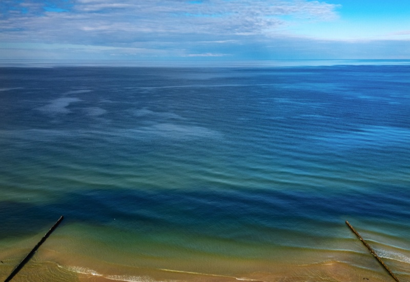 Spokojna piaszczysta plaża z delikatnymi falami i spokojnym błękitnym morzem pod niebieskim niebem z chmurami